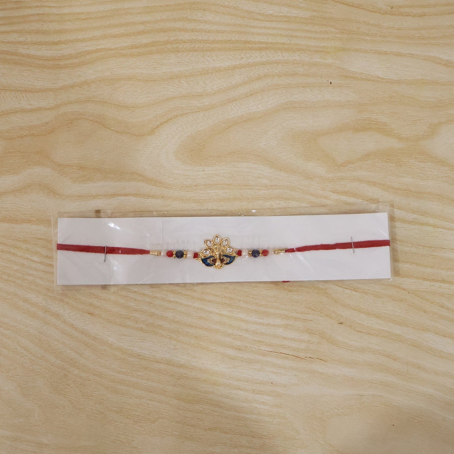 Decorative peacock rakhi with pearls and red thread