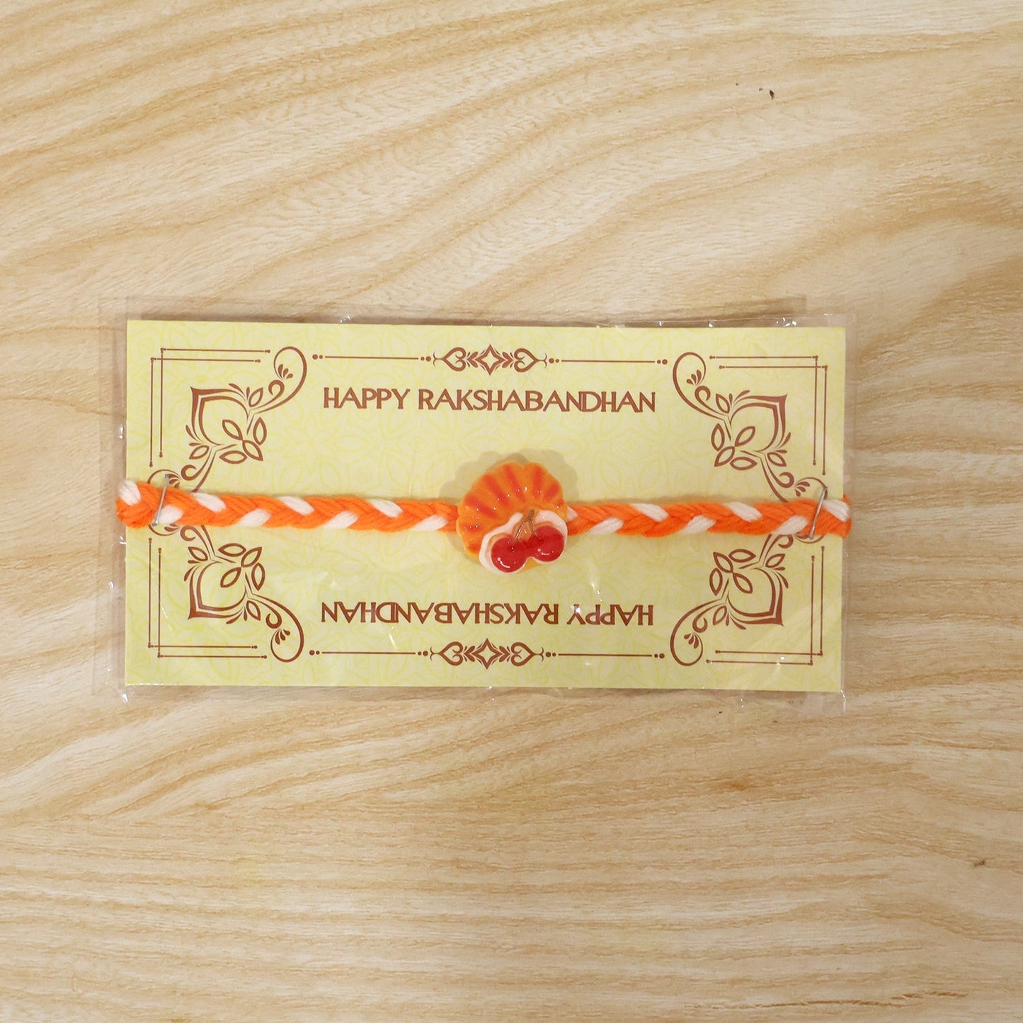 Close-up of the delicate thread and cherry pastry charm of the fancy Rakhi.