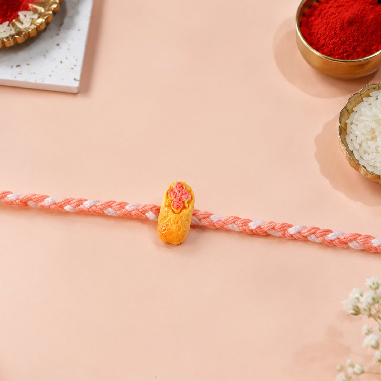 Top view of the stylish braided thread Rakhi with a fun cake charm.