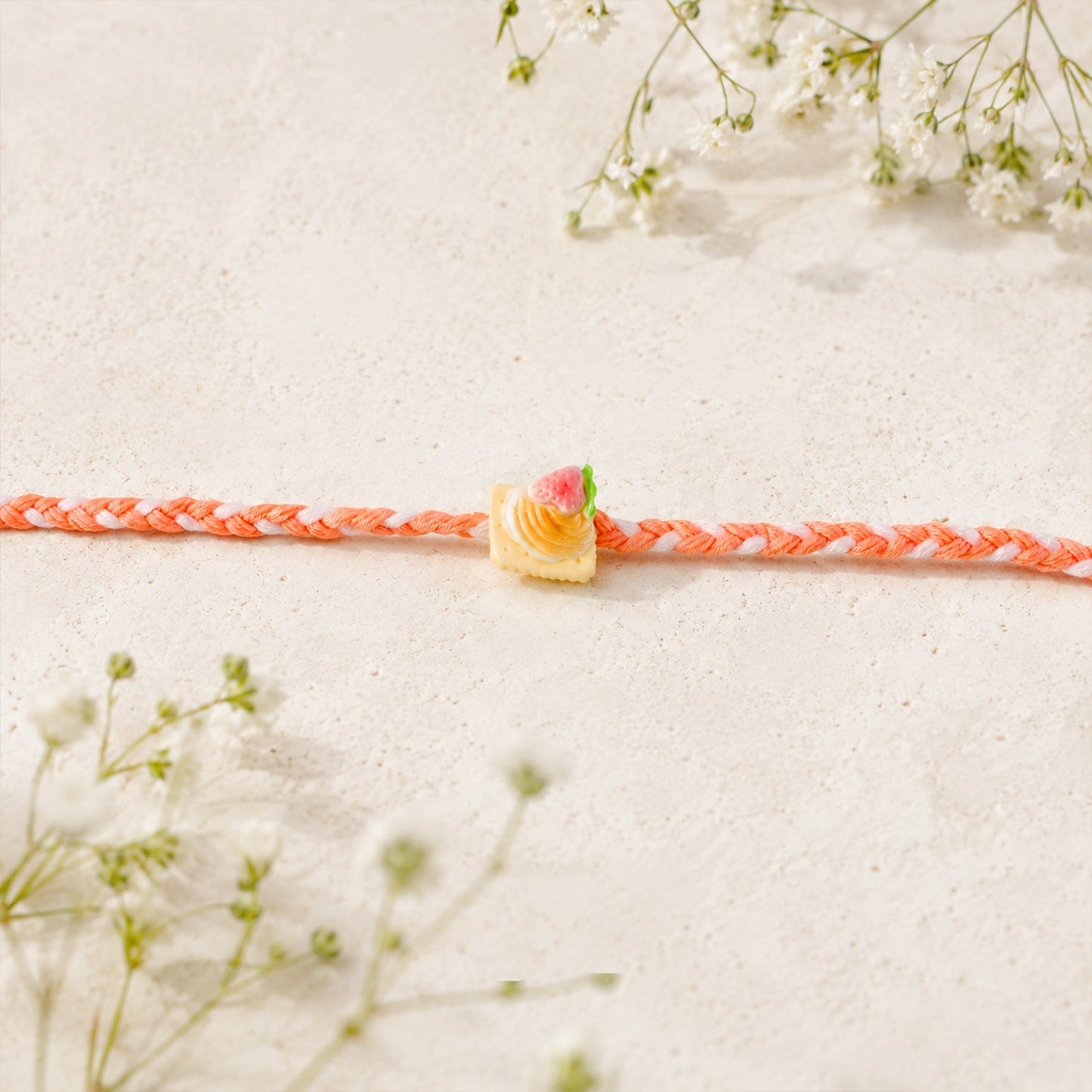 Close-up of strawberry biscuit charm on braided Rakhi