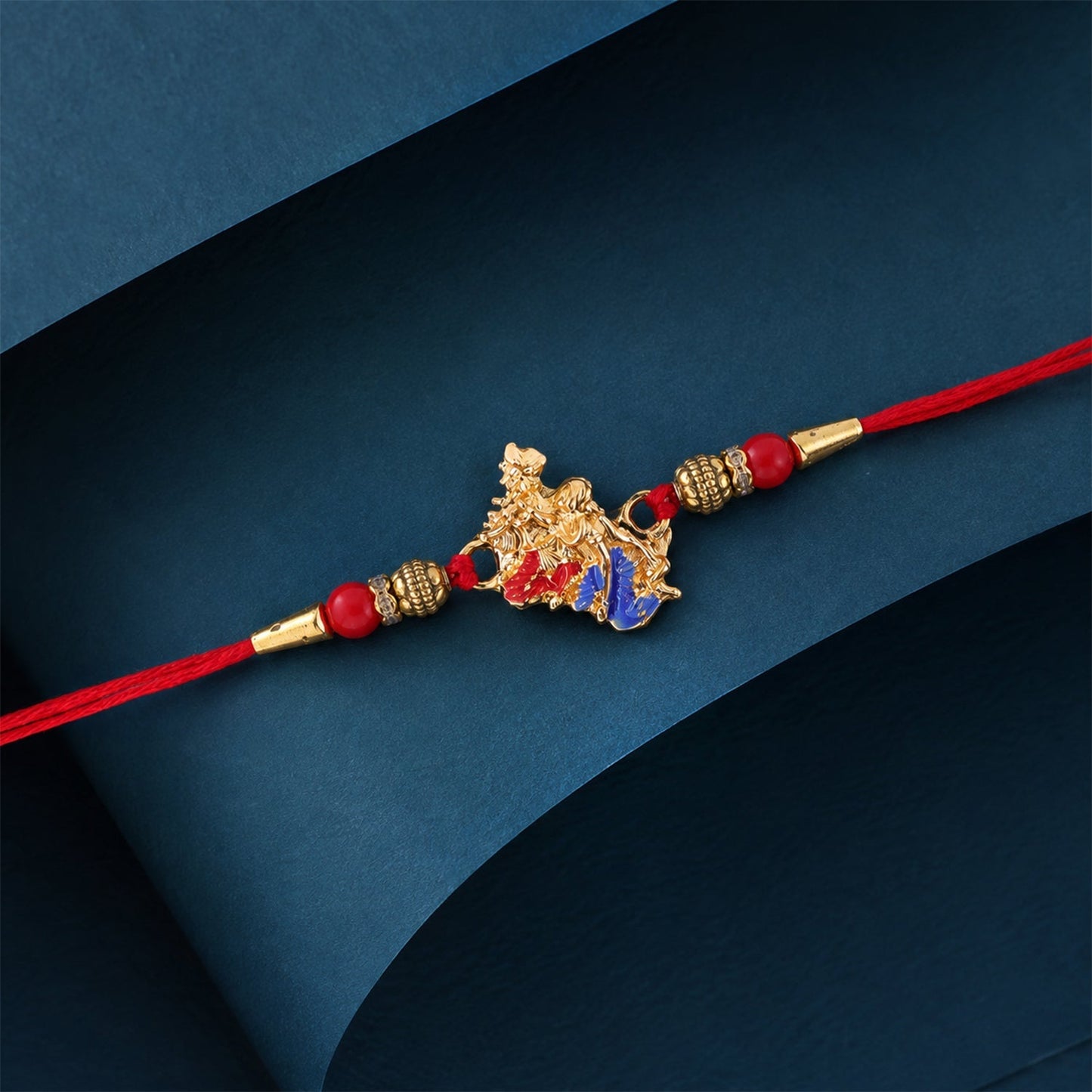 Close-up of a Golden Peacock Rakhi with blue enamel and red beads for brother