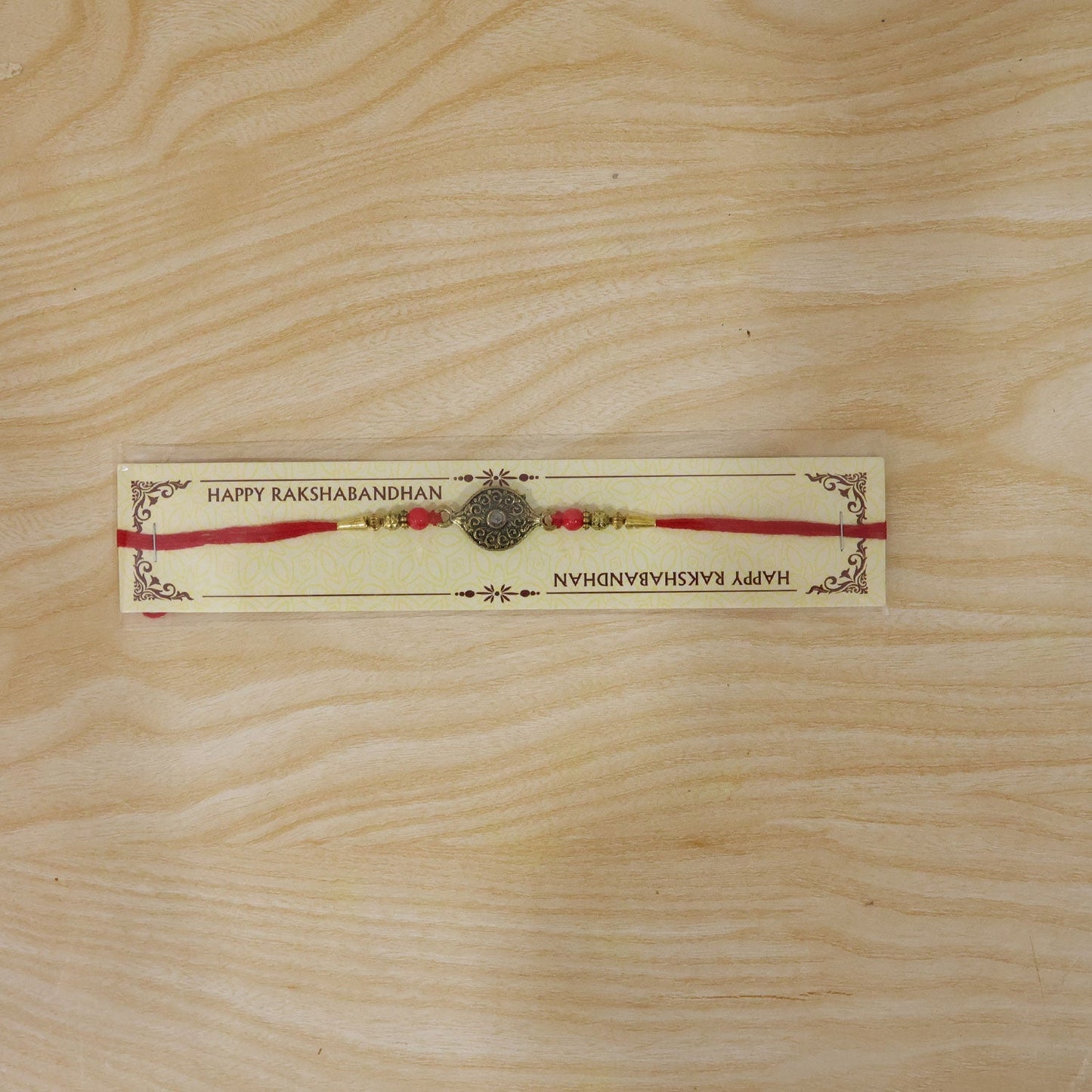 Antique oval Rakhi displayed on fabric with red beads